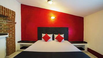 Quarto de hotel com parede de tijolos, parede de destaque vermelha, cabeceira preta, colcha branca e duas almofadas vermelhas.