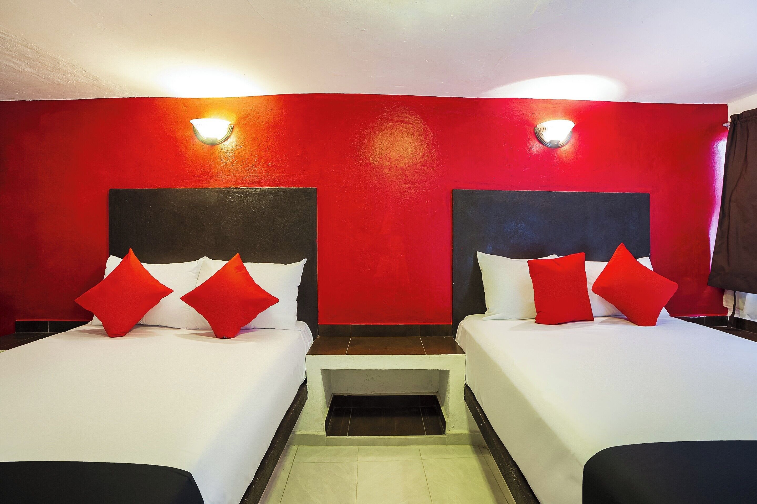 A hotel room with two beds, red walls, and a small wooden nightstand.