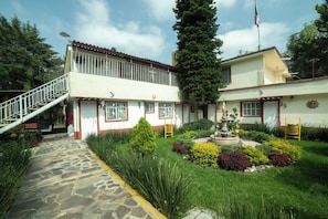 Un bâtiment à deux étages, avec un chemin de pierre menant à l’entrée, entouré de jardins bien entretenus et surmonté d’un mât.