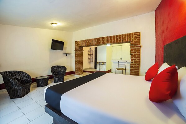 A hotel room with a bed, two wicker chairs, a small table, a TV, and a brick fireplace. - Capital O Hotel Meson Del Rio, Tepotzotlan (Tepotzotlán)
