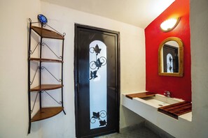 A bathroom with a white sink, a mirror with a wooden frame, a black door with a decorative design, and a metal shelf unit. - Capital O Hotel Meson Del Rio, Tepotzotlan (Tepotzotlán)
