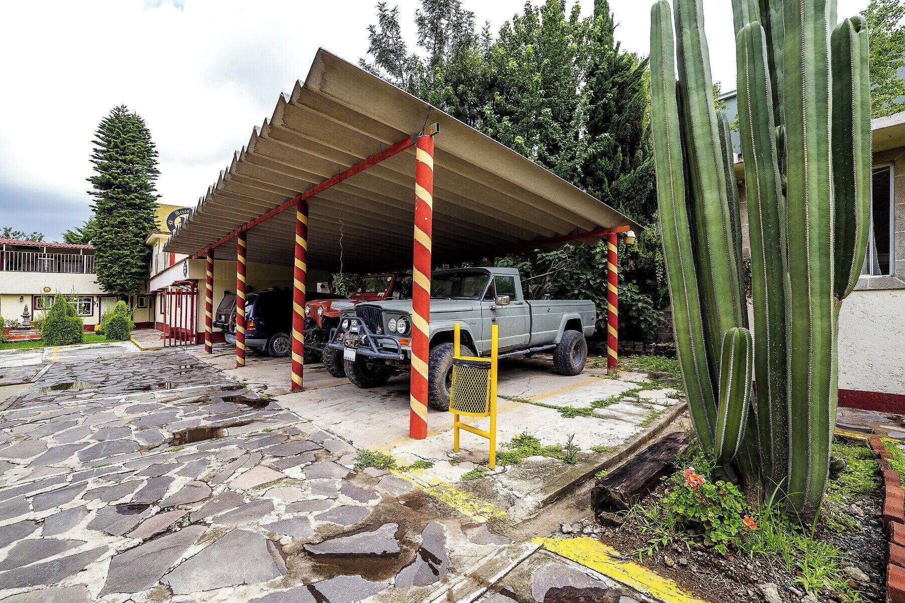 Un espace de stationnement doté d’une structure abritée, un camionnette et un grand cactus.