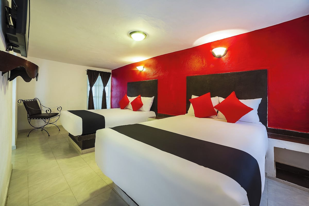 A hotel room with two beds, a chair, and a red accent wall.
