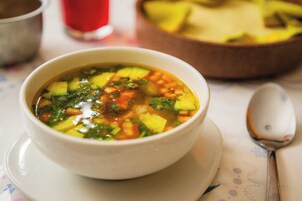 Un tazón de sopa sobre una mesa, con una cuchara y otro tazón al fondo.