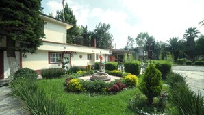 A building with a garden featuring a fountain, neatly trimmed hedges, and a flag. - Capital O Hotel Meson Del Rio, Tepotzotlan (Tepotzotlán)