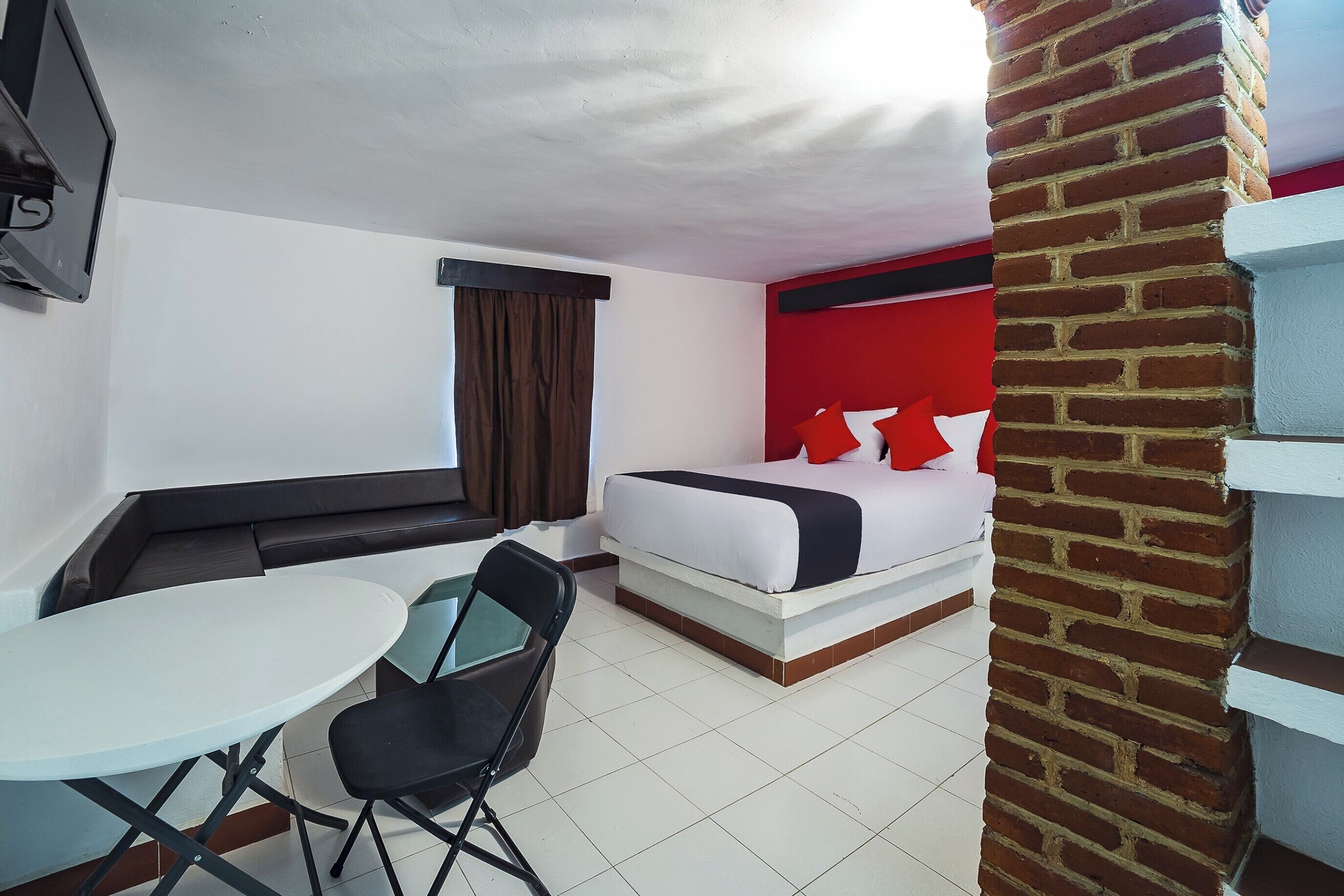 Una camera d'albergo con un letto, un tavolino, una sedia, una TV e una finestra con tende.