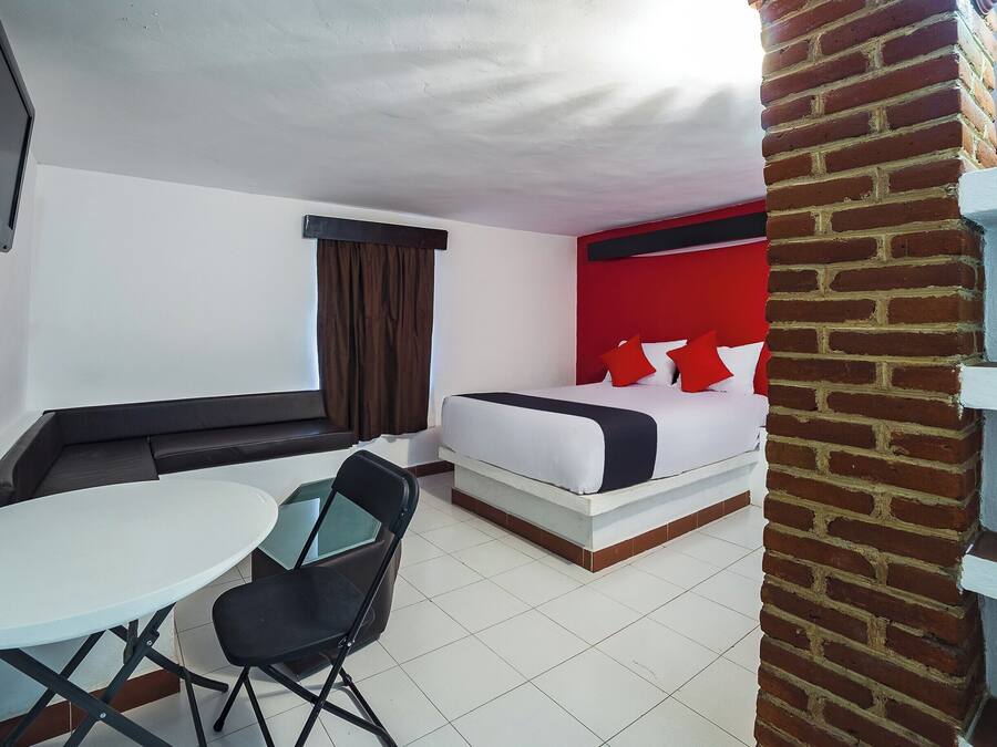 Una camera d'albergo con un letto, un tavolino, una sedia, una TV e una finestra con tende.
