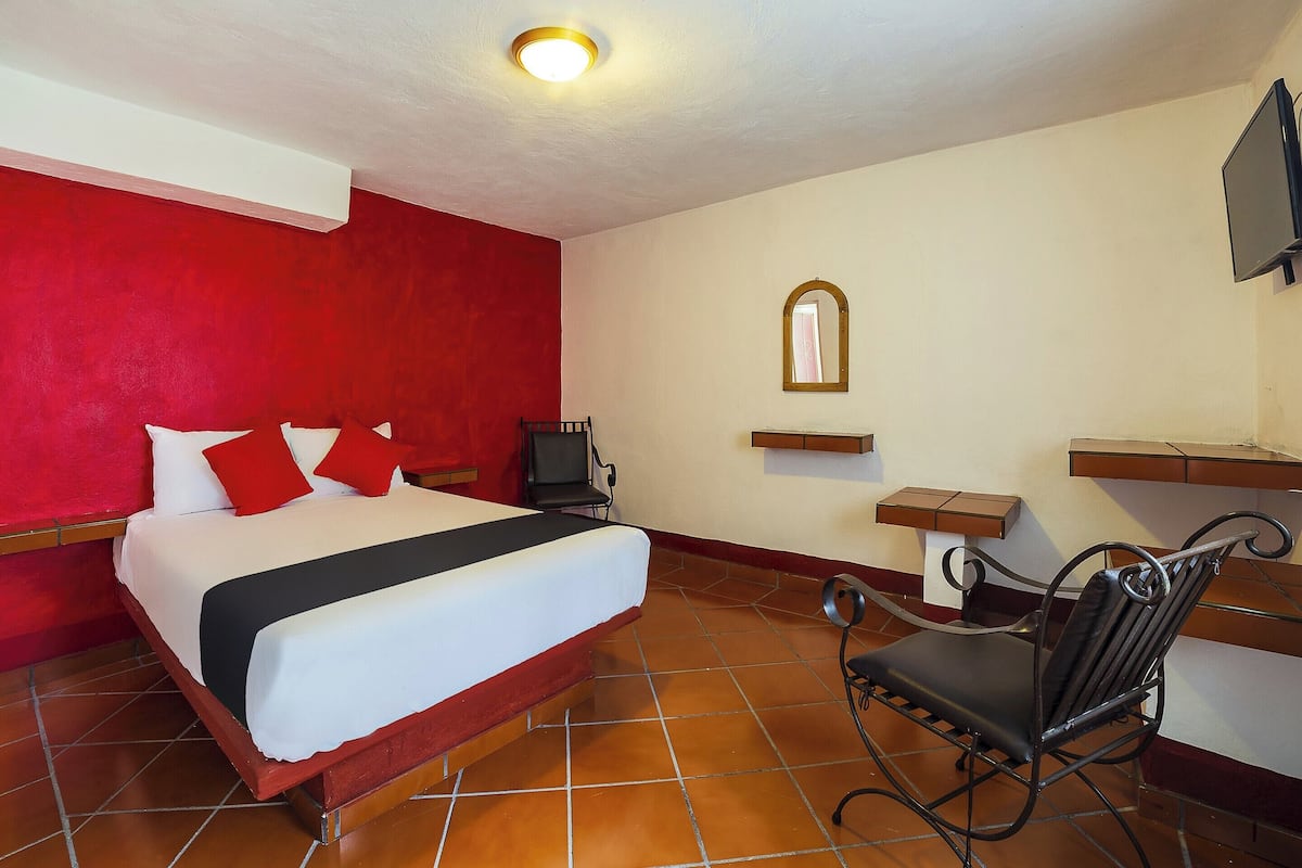 A hotel room with a bed, a desk, a chair, a television, and a mirror.
