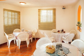 A dining area with white plastic chairs and tables, a basket with bread, and a cup of coffee.