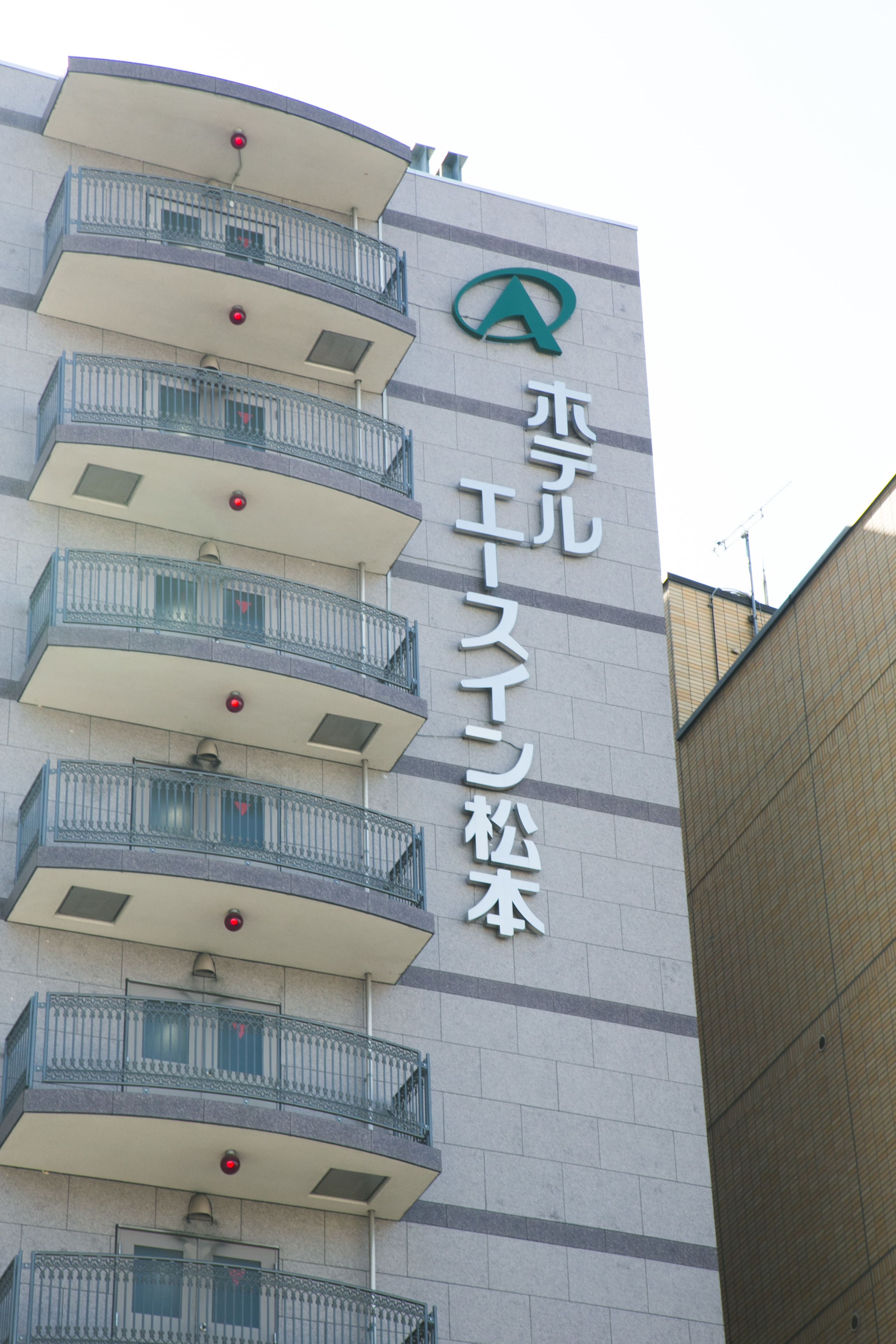 A building with a sign that reads "A" and Japanese characters. It has multiple balconies with railings and windows.