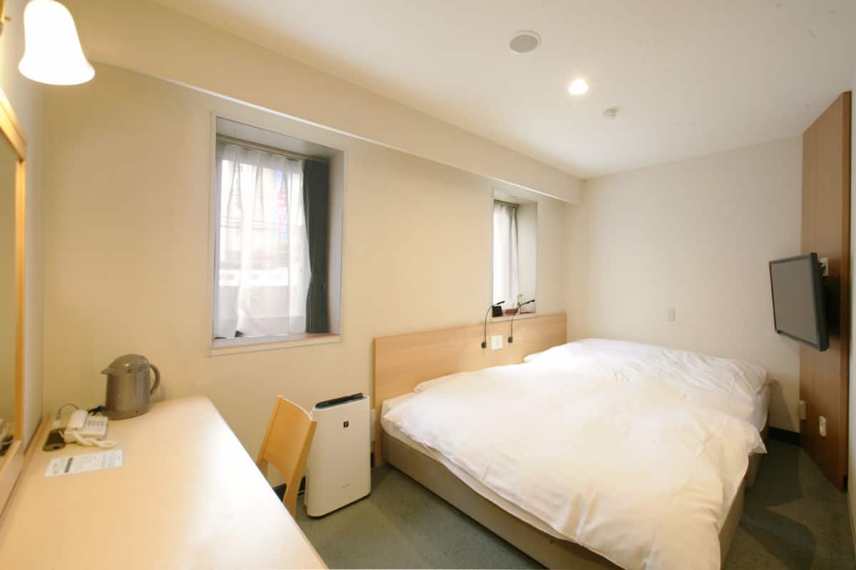 Ein Hotelzimmer mit Bett, Schreibtisch, Stuhl, kleinem Tisch, Wasserkocher, Fernseher und einem Fenster mit Vorhängen.