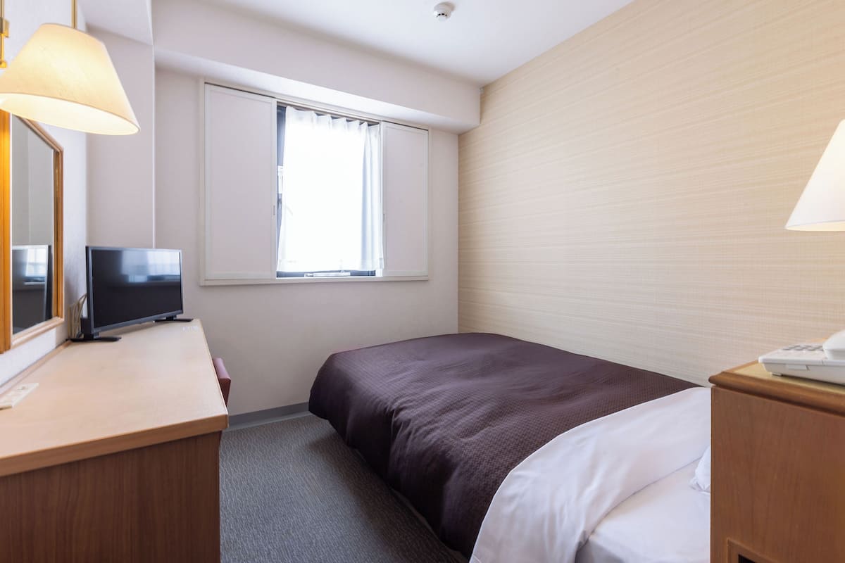 Ein Hotelzimmer mit einem Bett, einem Schreibtisch mit Fernseher, einem Fenster mit Vorhängen und einer Lampe.