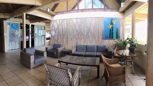 A lobby with wicker furniture, a blue sofa, and a painting of birds. - Hilo Reeds Bay Hotel (Hilo)
