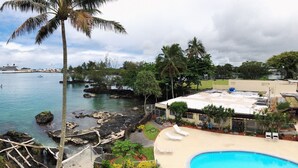 A pool area with lounge chairs, a view of the sea, and a building with a flat roof. - Hilo Reeds Bay Hotel (Hilo)