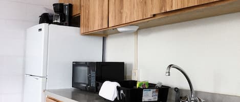 A compact kitchen with wooden cabinets, a white refrigerator, a black microwave, and a stainless steel sink.