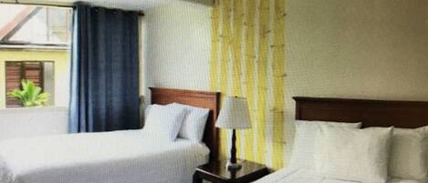 A hotel room with a bed, a nightstand, a lamp, and a window with curtains.