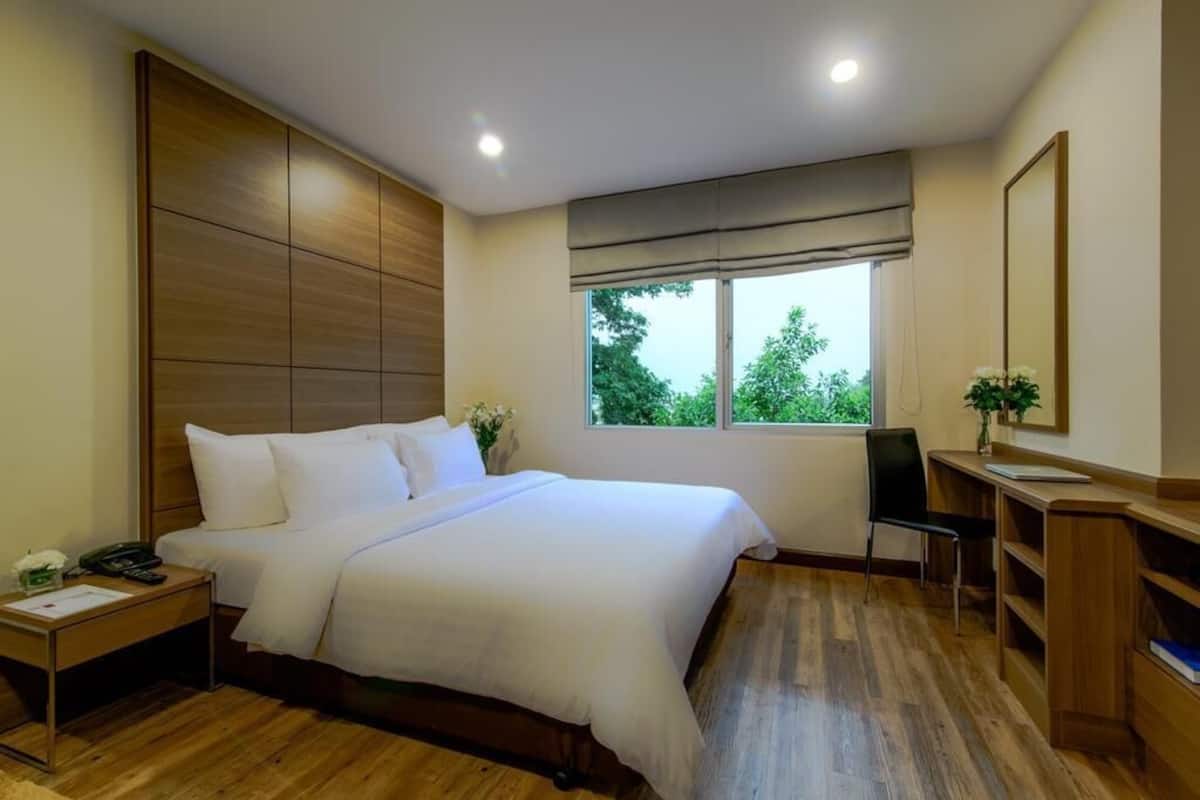 A bedroom with a large bed, bedside tables, a desk, and a window with a view of trees.