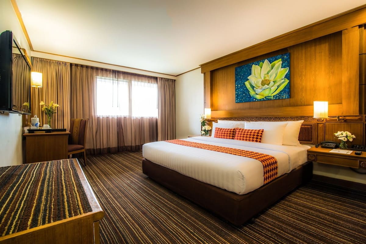 A hotel room with a large bed, a desk, a chair, a TV, and a painting of a lotus flower on the wall.