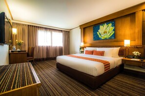Una habitación de hotel con una cama grande, un escritorio, una silla, un televisor y un cuadro de una flor de loto en la pared.
