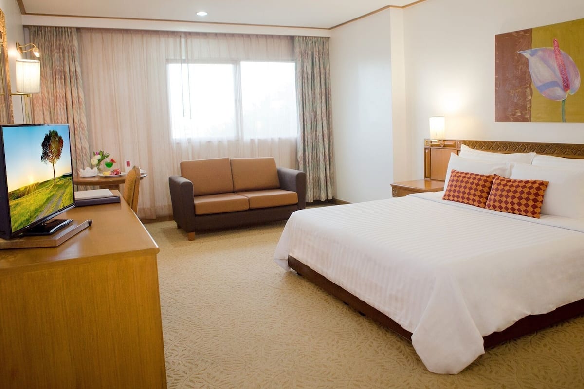 A hotel room with a large bed, a sofa, a desk with a TV, and a painting on the wall.