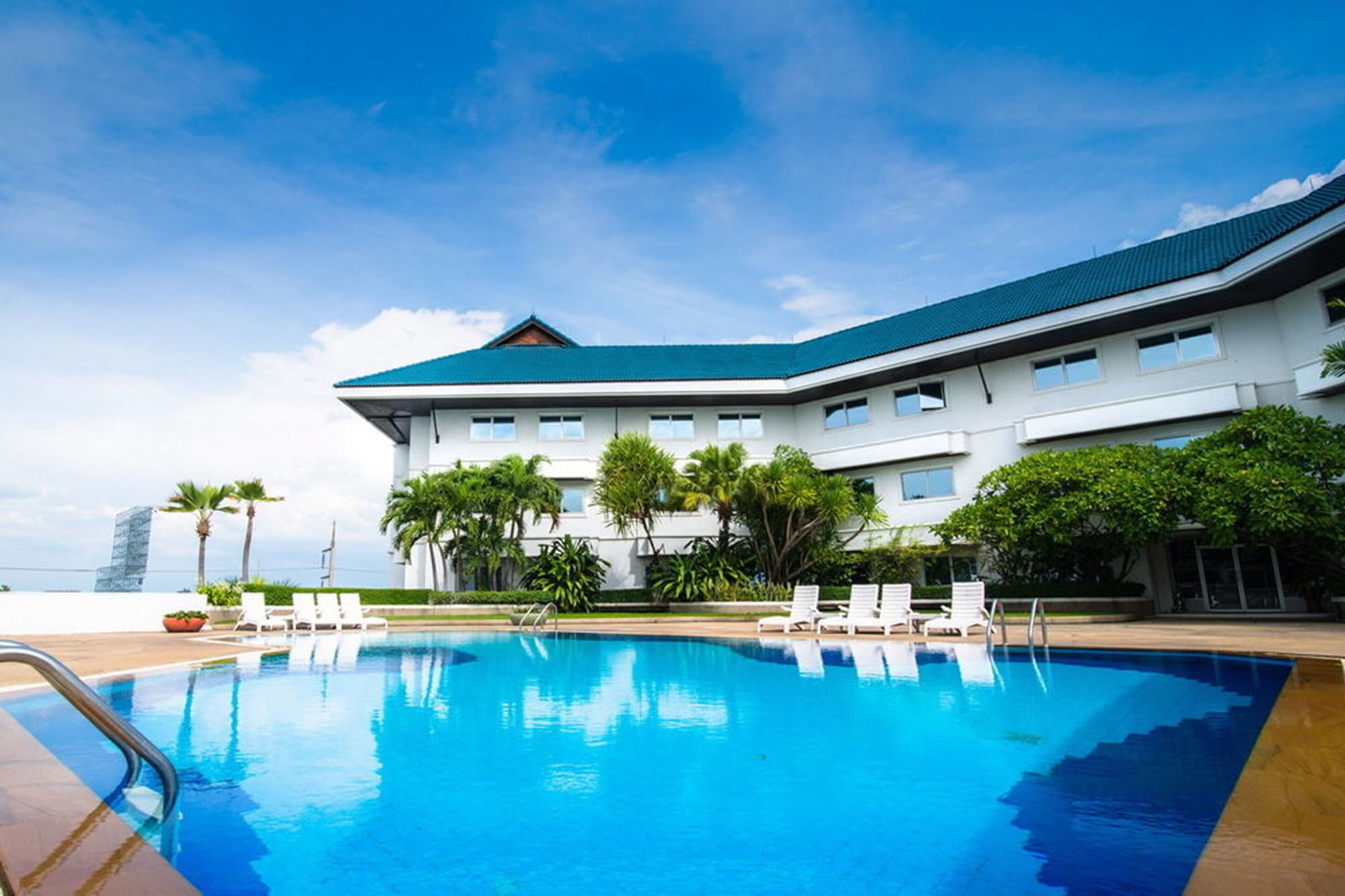 A hotel with a swimming pool, white exterior, and blue roof.