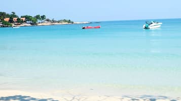Una playa con agua turquesa cristalina, un bote rojo y un bote blanco anclados cerca de la orilla.