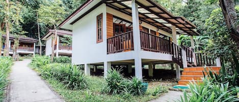 A two-story house with a balcony, surrounded by lush greenery.