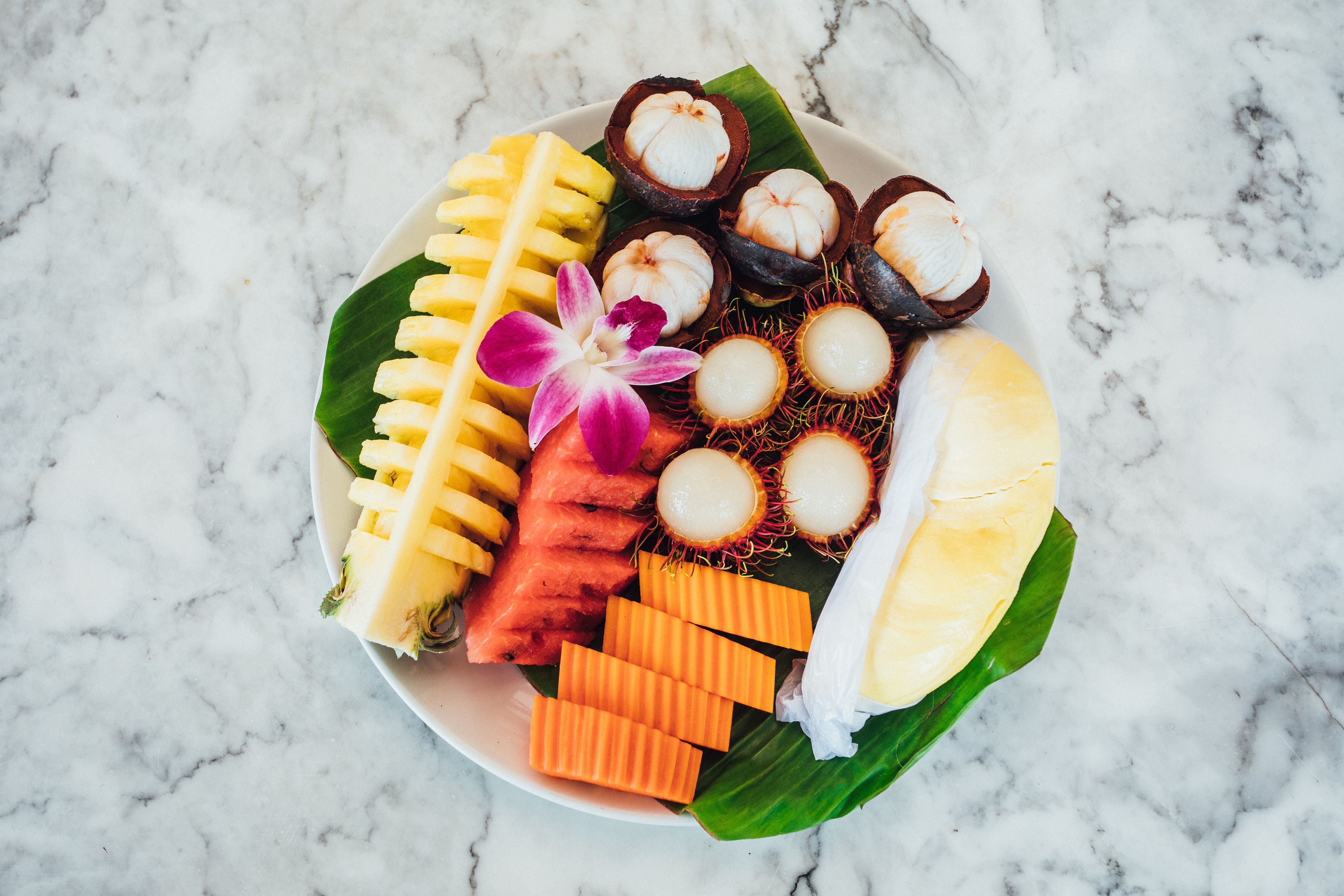 Een bord met diverse tropische vruchten en desserts op een marmeren oppervlak.