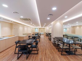 Un comedor amplio con varias mesas y sillas, suelo de madera e iluminación empotrada en el techo.