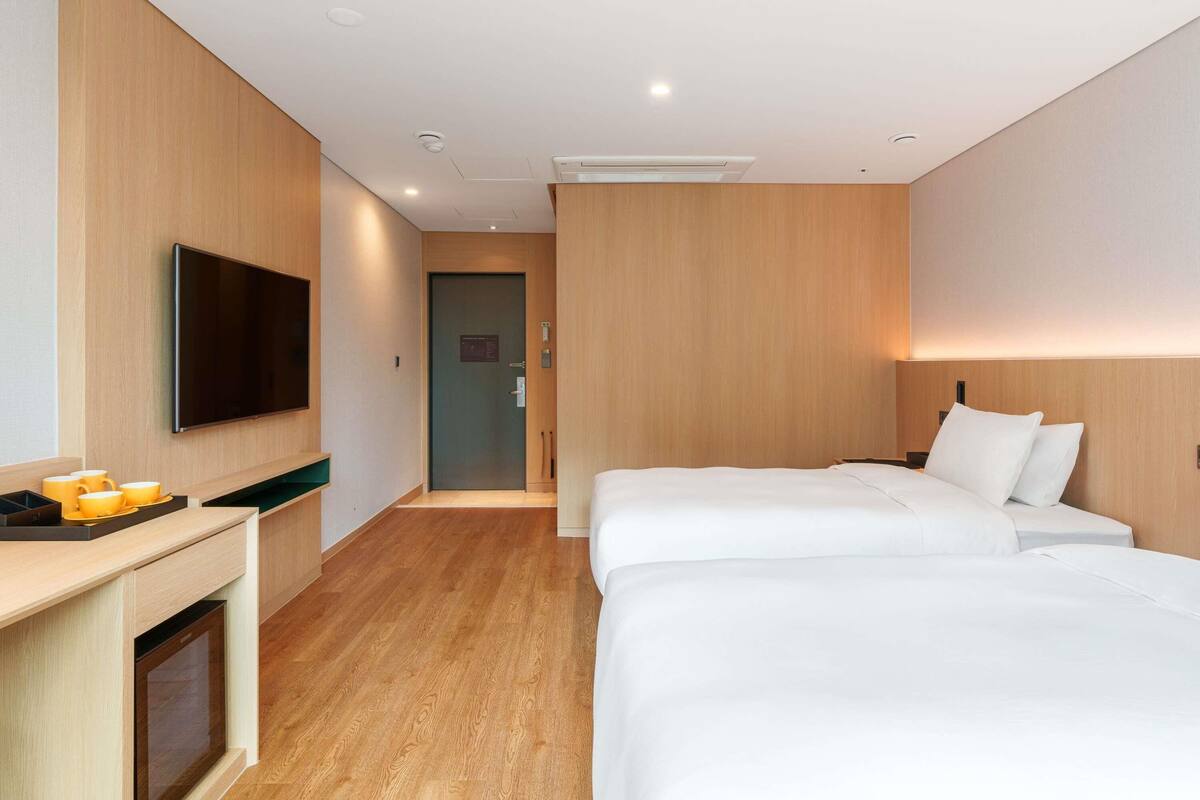 A hotel room with a flat-screen TV, two beds, a desk with a coffee maker, and a built-in oven.