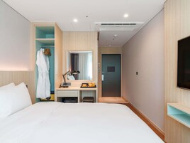 Habitación de hotel con cama, escritorio con lámpara, bata y televisor en la pared.