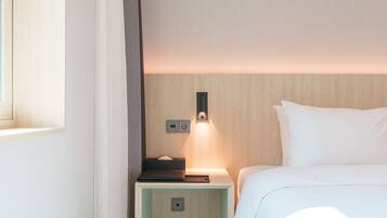 Una habitación de hotel con cama, mesita de noche, lámpara y luz empotrada en la pared.