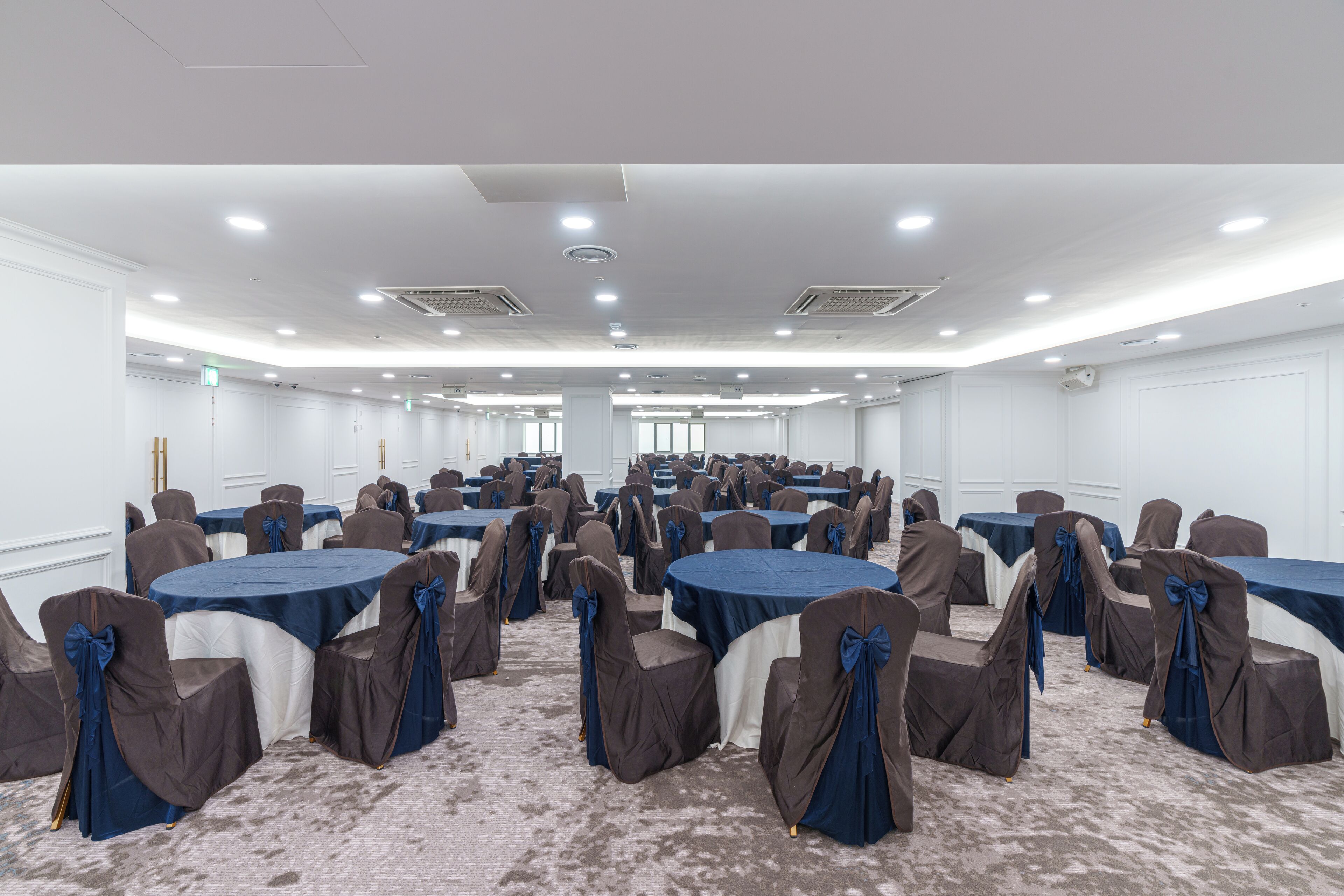 A conference room with multiple round tables and chairs, white walls, and ceiling lights.