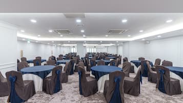 A conference room with multiple round tables and chairs, white walls, and ceiling lights.