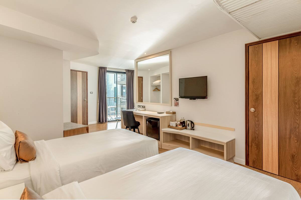A hotel room with two beds, a desk, a chair, a television, and a wardrobe.