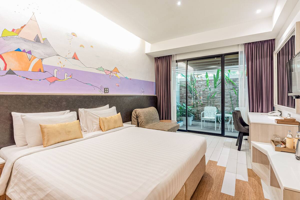 A modern hotel room with a large bed, a desk, and a view of the outdoors.