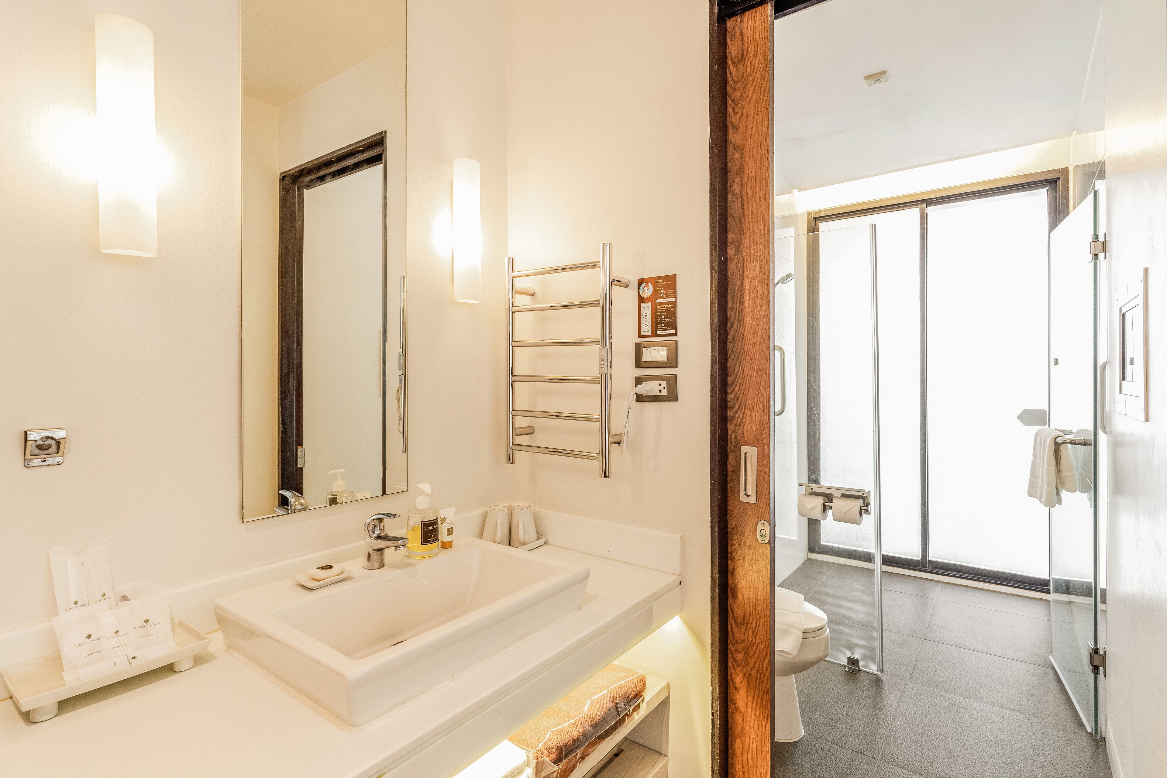 A modern bathroom with a large mirror, white sink, and a glass shower door.