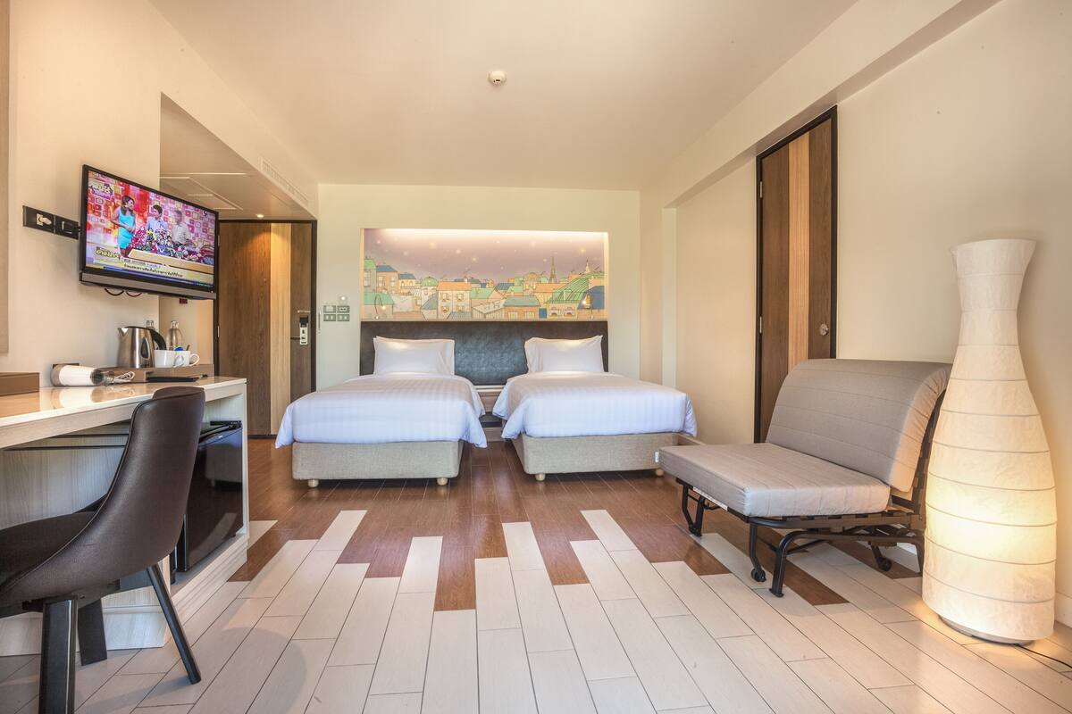 A hotel room with two beds, a desk with a chair, a television, and a large vase.