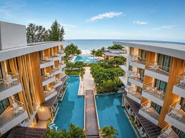 Un hotel de varios niveles con piscina central, balcones con mobiliario exterior y vistas al océano.