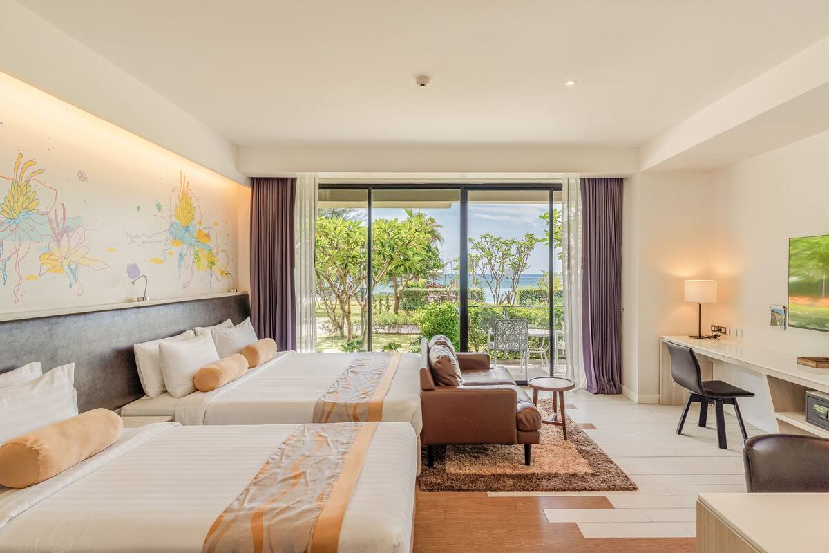 A hotel room with two beds, a desk, a chair, a sofa, and a view of the outdoors.