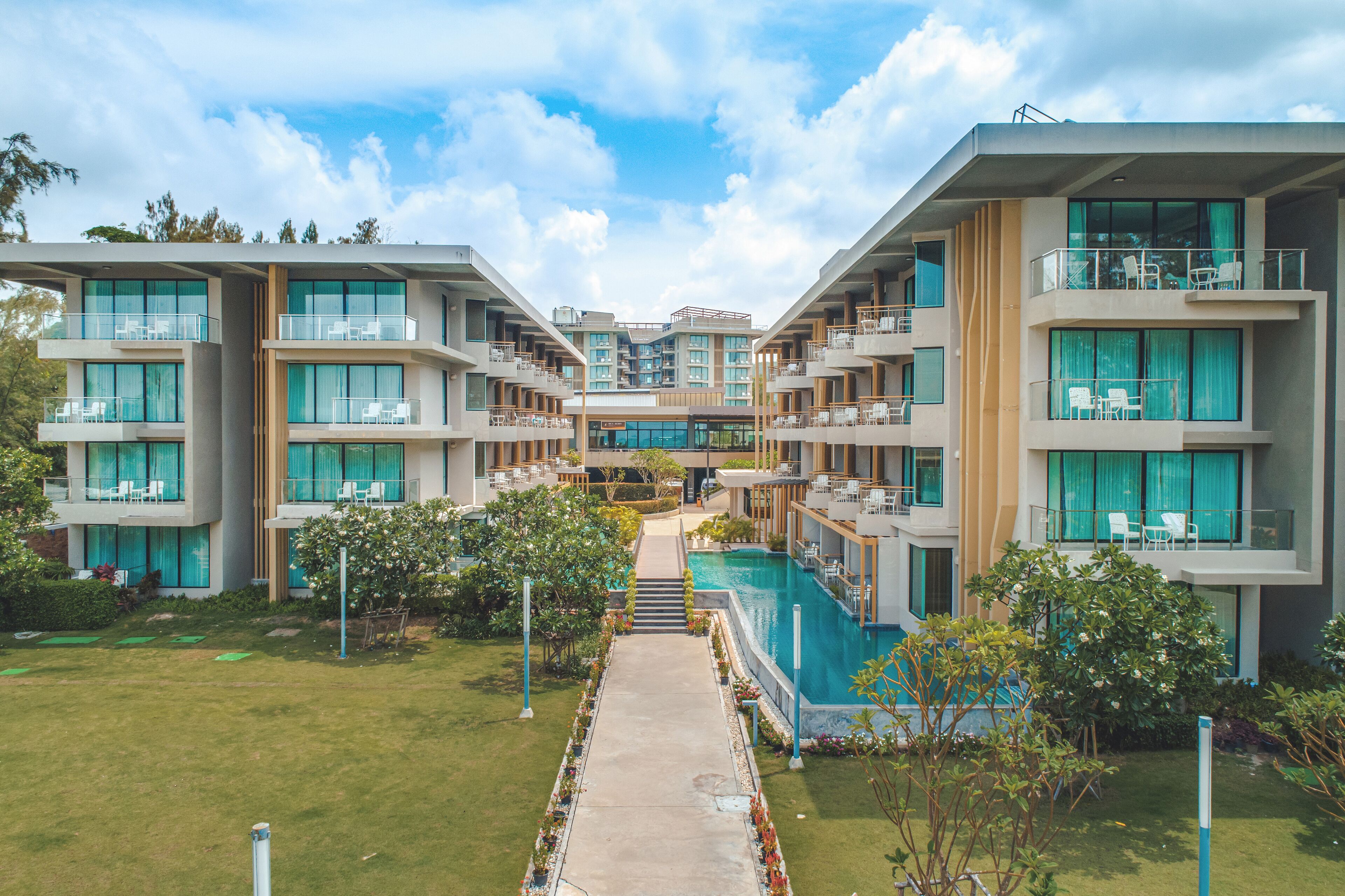 A modern hotel with multiple balconies, a central pool, and a well-maintained garden.