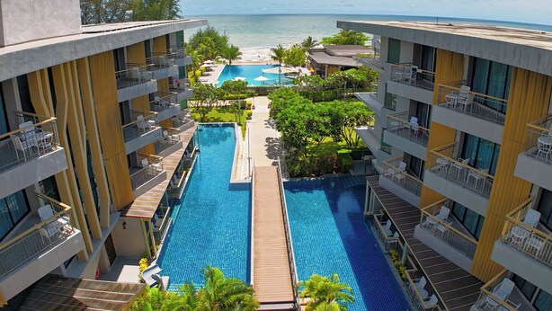 A hotel with a central swimming pool, multiple balconies, and a view of the ocean. - Sand Dunes Chaolao Beach Resort (Tha Mai)