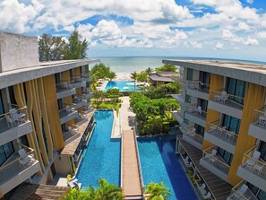 A hotel with a central swimming pool, multiple balconies, and a view of the ocean. - Sand Dunes Chaolao Beach Resort (Tha Mai)