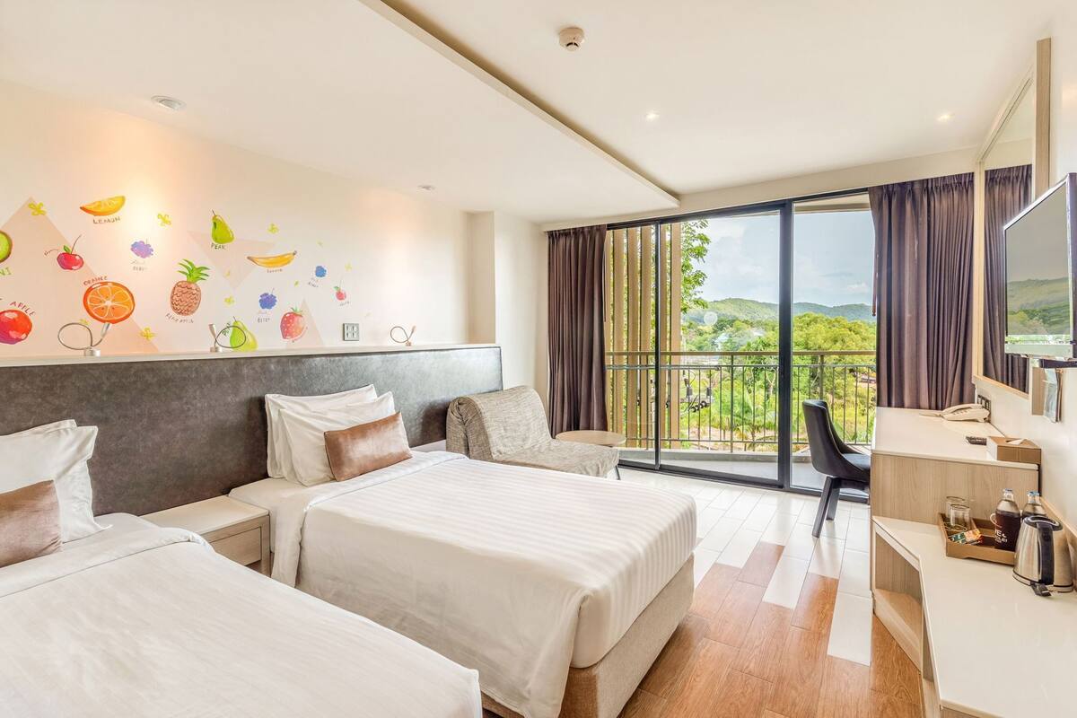 A hotel room with two beds, a desk, a chair, and a balcony with a view.