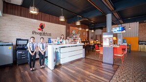 A reception desk with a logo, a counter, and a seating area with chairs and tables. - Prajaktra City Hostel (Udon Thani)