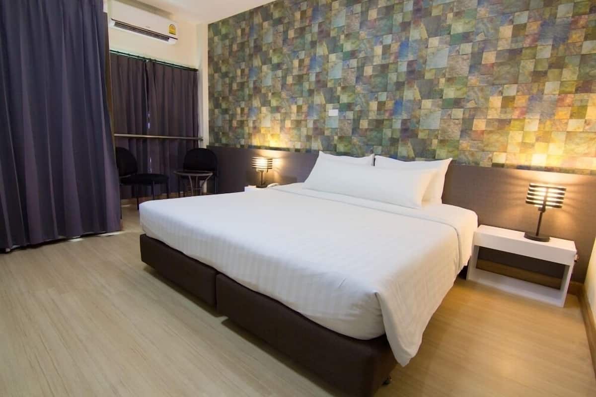 A hotel room with a large bed, two bedside tables with lamps, a wall with a mosaic pattern, and a dark curtain.