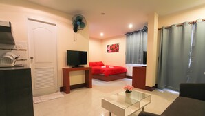 A modern living room with a sofa, a glass coffee table, a TV, and a red bed. - Walking Street Guest House (Pattaya)
