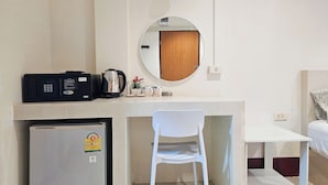 A compact room with a kitchenette, a small refrigerator, a white chair, a bedside table, and a bed. - Walking Street Guest House (Pattaya)