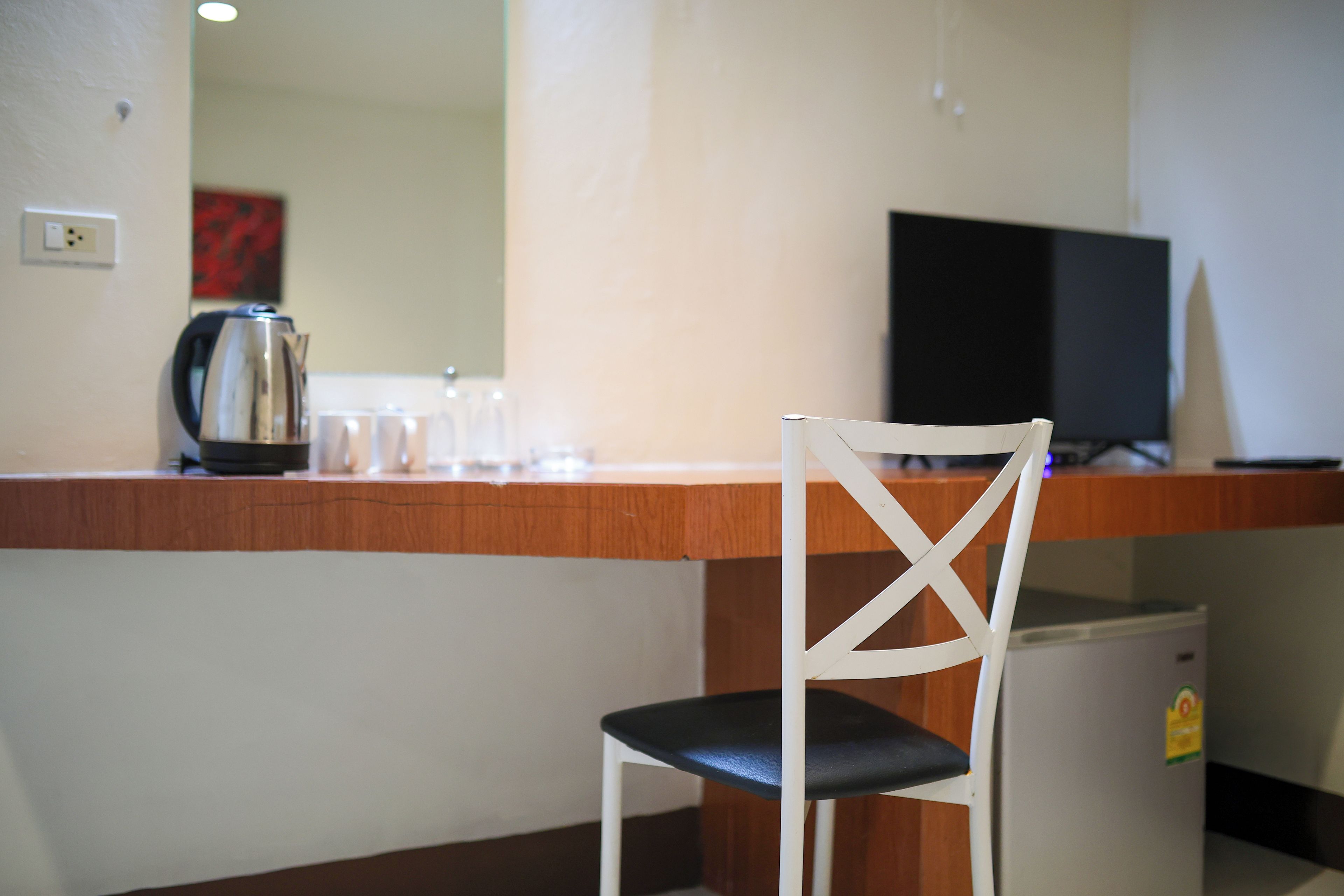 A hotel room with a wooden desk, a television, a small refrigerator, and a white chair.