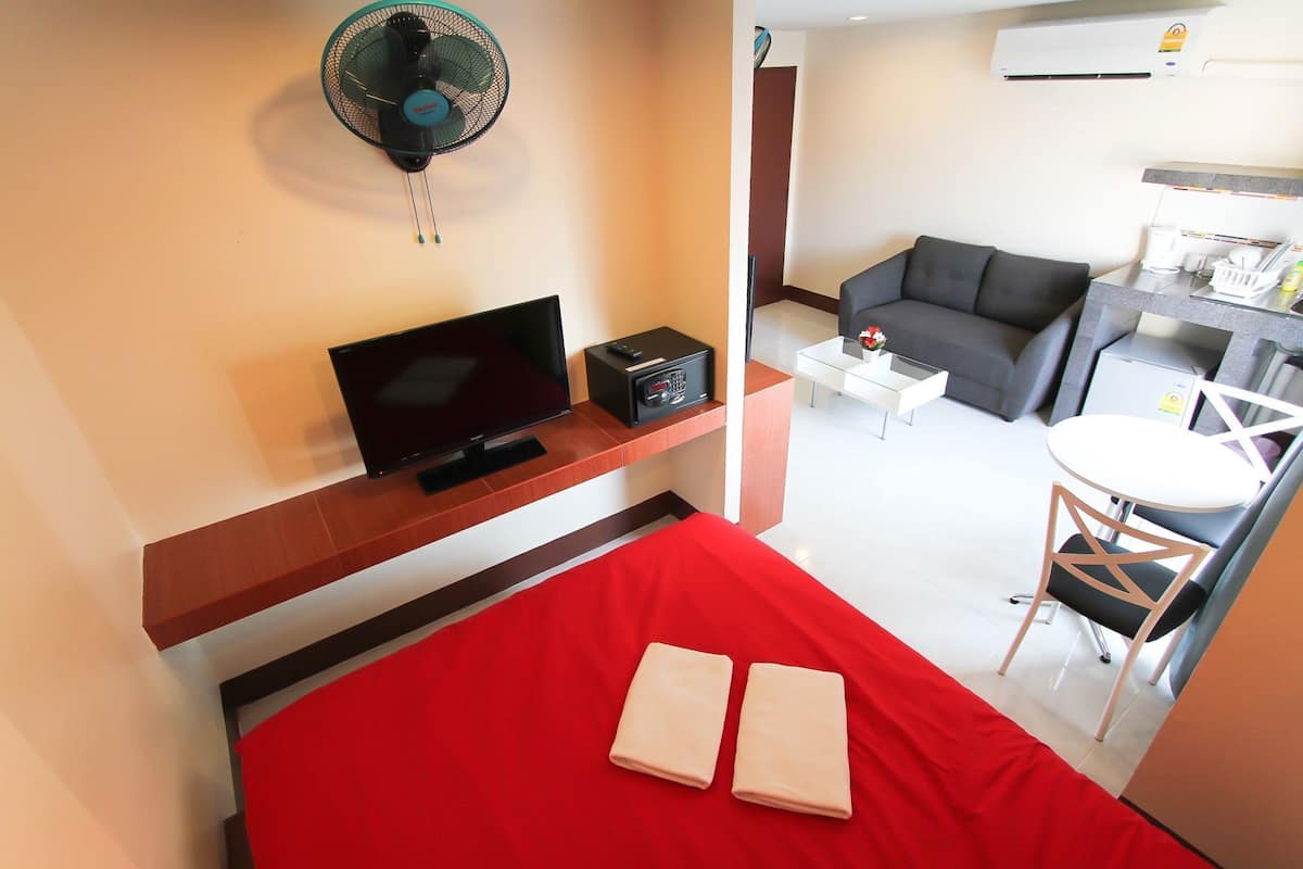 Hotellihuone, jossa on sänky, televisio, tuuletin, sohva, pieni pöytä ja pieni keittiö.